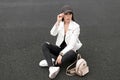 Young cute woman in vintage ripped jeans in a leather jacket in a t-shirt with a gold backpack in fashionable sneakers Royalty Free Stock Photo