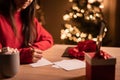 Young cute woman wearing red sweater writing greeting cards or letter late evening at home office during christmas Royalty Free Stock Photo