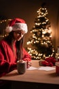 Young cute woman wearing red sweater writing greeting cards or letter late evening at home office during christmas. Royalty Free Stock Photo