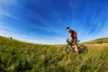 Young cyclist cycling on the green meadow against beautiful blue sky with clouds in the countryside. Royalty Free Stock Photo