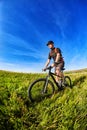 Young cyclist riding mountain bicycle through green meadow against beautiful sky. Royalty Free Stock Photo