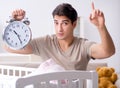 Young dad with clock near newborn baby bed cot Royalty Free Stock Photo