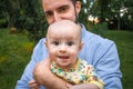 Young dad holds his baby son in his arms close-up outdoors. Kid looking at the camera and stuck out his tongue Royalty Free Stock Photo