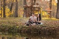 Young dad and mom with baby girl and little son having fun on blanket near pond in autumn park on sunny day. happy family concept Royalty Free Stock Photo