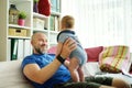 Young dad works remotely from home office with baby. Freelancer man holding his infant while using laptop. Workplace in living Royalty Free Stock Photo