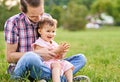 Young daddy sitting in a park in the grass with his little toddler daughter on his lap - 20s husband plays with his child and Royalty Free Stock Photo