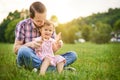 Young daddy sitting in a park in the grass with his little toddler daughter on his lap - 20s husband plays with his child and Royalty Free Stock Photo