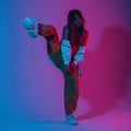 Young dancer in a stylish top in a hoodie in trendy pants in sneakers posing on one leg in a room with bright pink ultraviolet Royalty Free Stock Photo