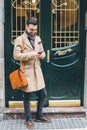 Young dandy man using his smartphone on the street at the front door