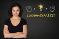 Young woman with crossed arms, heads, bulb-idea & text `Zusammenarbeit`on a blackboard. Translation: & x27;Teamwork& x27; Royalty Free Stock Photo