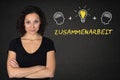 Young woman with crossed arms, heads thinking, lightbulb-idea and text `Zusammenarbeit` on a blackboard. Trans: Teamwork Royalty Free Stock Photo