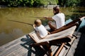 Young dark-haired father and his little son are sitting in recliners on the wooden pier with fishing rods and fishing. Royalty Free Stock Photo