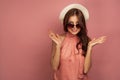Young brunette with a straw hat spreads out her hands smiling at the camera, pink background Royalty Free Stock Photo