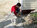 A young dark-haired guy in daily clothes hammers a rubber mallet over the surface of paving slabs. The concept of self-laying Royalty Free Stock Photo