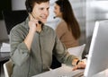 Young dark-haired guy in a green shirt and headsets is talking to a client, while sitting at the desk, working together Royalty Free Stock Photo