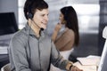 Young dark-haired guy in a green shirt and headsets is talking to a client, while sitting at the desk, working together Royalty Free Stock Photo