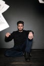 A young dark-haired man with a beard sits on the floor and throws papers and documents into the air. Human emotions