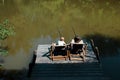 A young dark-haired man and a blond boy are sitting in recliners on the wooden pier with fishing rods and fishing. Royalty Free Stock Photo