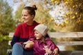 Young dark haired mother with daughter sitting on wooden bench in autumn park near lake or river, family having rest by water, mom Royalty Free Stock Photo