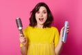 Young dark haired woman wears yellow shirt holds hair brush and hair spray. Attractive lady looks surprised. Female with rose Royalty Free Stock Photo