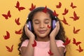 Young dark skinned  girl with long curly hair  in headphones enjoying music on a yellow background. Hand-drawn red butterflies fly Royalty Free Stock Photo