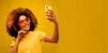 Young dark skinned happy mulatto woman with Afro hairstyle, holds modern mobile phone in front of face Royalty Free Stock Photo