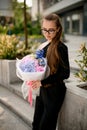 Young darkhair girl in black outfit holding huge bouquet of different fresh flowers in wrapping paper on blurred