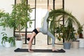 Young darkhair woman practicing yoga in the morning at her home near plants. The woman is engaged in self-determination