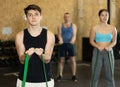 Motivated young man practicing exercises with stretch rope standing near other people in gym Royalty Free Stock Photo