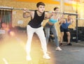Motivated young man practicing exercises with rod near other people in gym Royalty Free Stock Photo