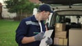 Young delivery man checking delivery list. Delivery man in cap and documentation in hands outdoor. Courier with parcel