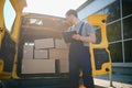 young delivery man courier in uniform hold documents clipboard checking list parcel post boxes near a car for service Royalty Free Stock Photo