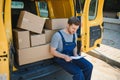 young delivery man courier in uniform hold documents clipboard checking list parcel post boxes near a car for service Royalty Free Stock Photo