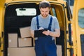 young delivery man courier in uniform hold documents clipboard checking list parcel post boxes near a car for service Royalty Free Stock Photo