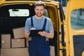 young delivery man courier in uniform hold documents clipboard checking list parcel post boxes near a car for service Royalty Free Stock Photo