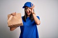 Young delivery woman with blue eyes wearing cap holding paper bag with food with happy face smiling doing ok sign with hand on eye Royalty Free Stock Photo