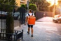 Young deliveryboy walking with red thermal bag on city street. Man of delivery service in hurry to deliver an order. Royalty Free Stock Photo