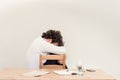 Young, depressed Caucasian freelancer man sitting in his home office at the table in front of empty clear wall. Royalty Free Stock Photo