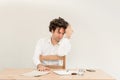 Young, depressed Caucasian freelancer man sitting in his home office at the table in front of empty clear wall. Royalty Free Stock Photo