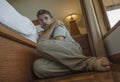 Young depressed and desperate man sitting on bedroom floor next to bed suffering depression and anxiety feeling overwhelmed and Royalty Free Stock Photo