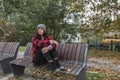 Young depressed homeless girl or woman with hat sitting alone on the bench on the street in the cold weather feeling desperate and Royalty Free Stock Photo