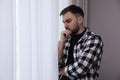 Young depressed man near window at home, space for text Royalty Free Stock Photo