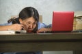 Young depressed and stressed Asian Chinese student girl working with laptop and book pile overwhelmed and frustrated preparing exa Royalty Free Stock Photo