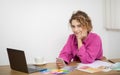 Young designer woman sitting at desk with colour swatches and using smartphone