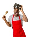 Young desperate and confused black afro american man in chef apron holding cooking pot in his head Royalty Free Stock Photo