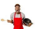 young desperate and confused black afro american man in chef apron holding cooking pot and spoon in his hands looking lost