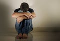 Young desperate and depressed man crying alone sitting at home floor in shady and dramatic studio light looking sad and frustrated Royalty Free Stock Photo