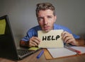 Young desperate and stressed businessman feeling overwhelmed working with laptop computer at office desk sad suffering stress aski Royalty Free Stock Photo