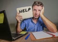 Young desperate and stressed businessman feeling overwhelmed working with laptop computer at office desk sad suffering stress aski Royalty Free Stock Photo