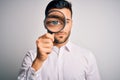 Young detective man looking through magnifying glass over isolated background with a confident expression on smart face thinking